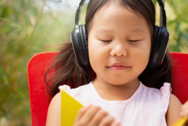 Photo of a young child wearing large headphones listening to music whilst holding a book