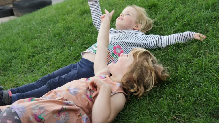 Two early years children lying on the grass looking up at the sky