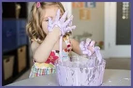 An early years child with her hands in a sticky substance in a bowl