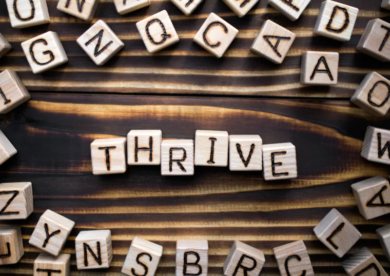 Scrabble letters spell out the word THRIVE on a wooden background