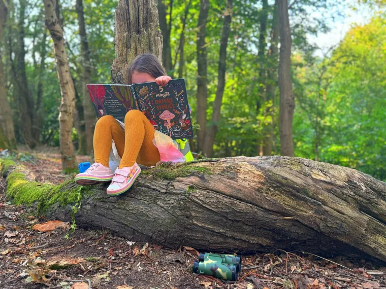 A picture of a child reading on a log in the woods