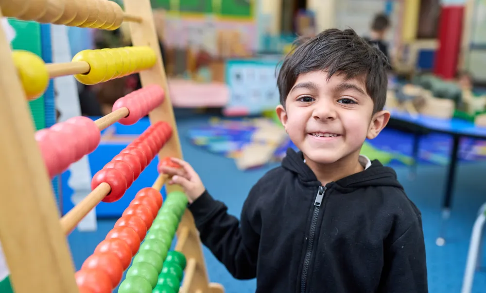 young boy smiling at the camera in front of a large abacus
