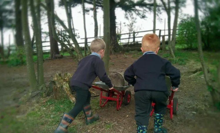 Children pushing wheelbarrows up a hill in a woodland environment