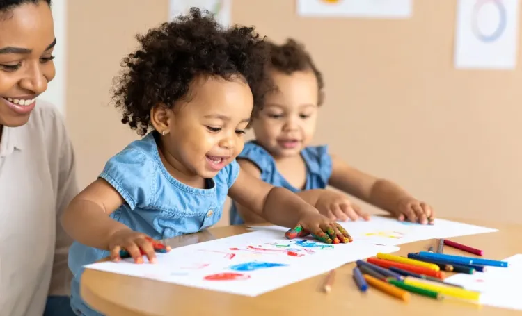 Babies with an adult drawing with crayons on paper