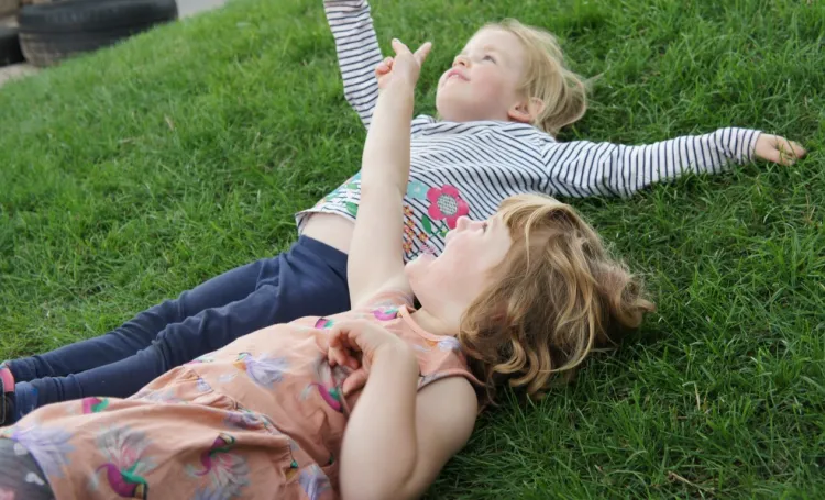 Two early years children lying on the grass looking up at the sky