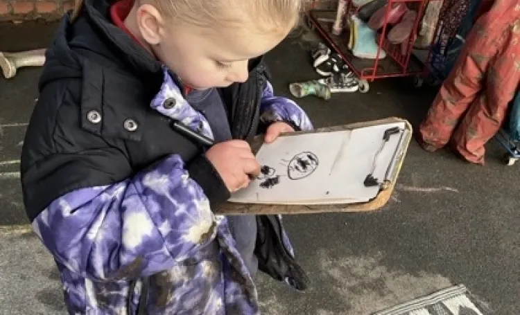 Child writing on a clipboard in an outdoor play area.
