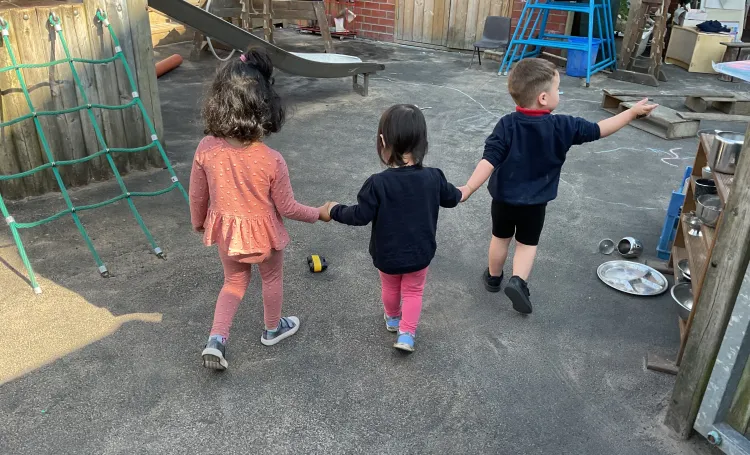Three children holding hands in an outdoor play area. 