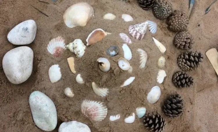 Image shows a spiral of shells and stones on sand at the beach.