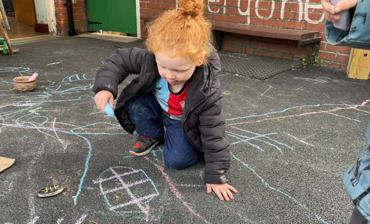 A child drawing and making marks on the floor outside using chalk