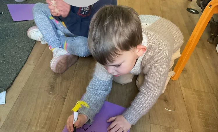 A child writing on a piece of purple paper, kneeling down. 