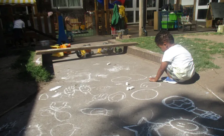 Child playing outdoors drawing with chalk