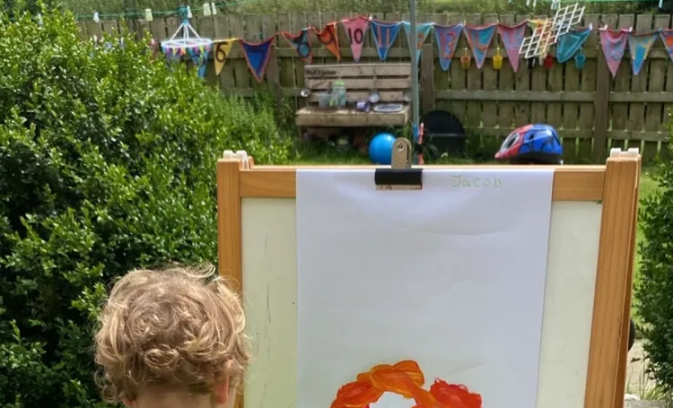 A child painting at an easel in a garden with views into the countryside. 