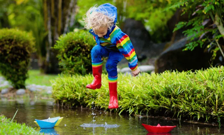 toddler in raincoat and wellies jumping in a puddle