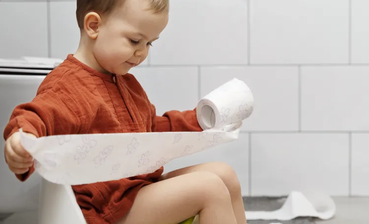 young boy sitting on a potty holding toilet paper