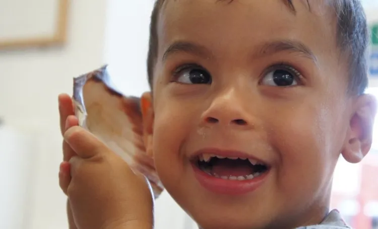 Child putting a shell to their ear to listen